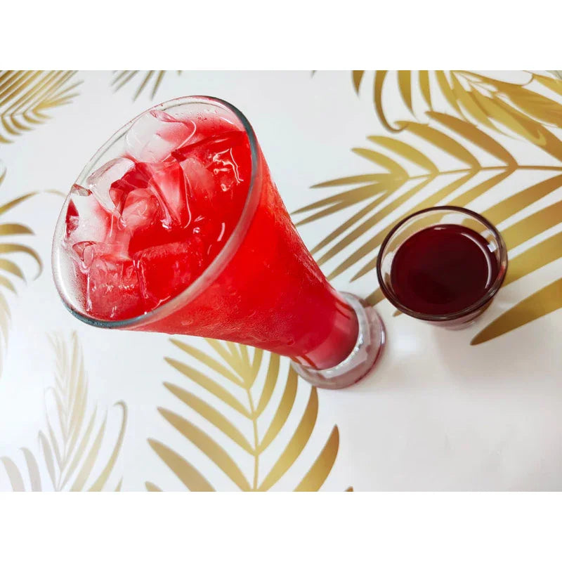 Verre de boisson rouge aux glaçons avec petit verre de sirop de fruit fraise sur table décorée feuilles dorées