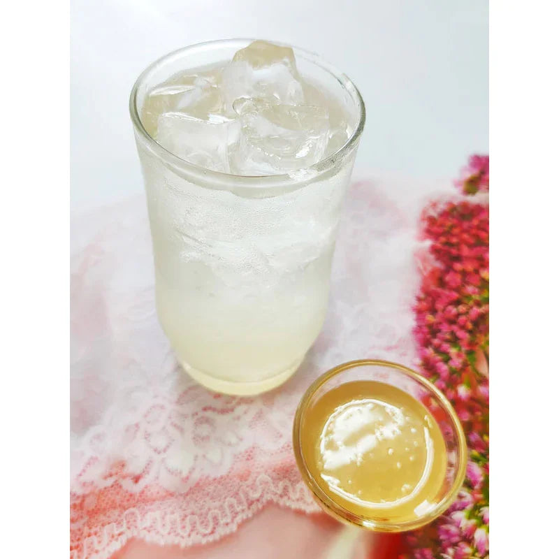 Verre de boisson glacée claire avec cubes de glace et petit bol de sirop doré sur nappe dentelle rose