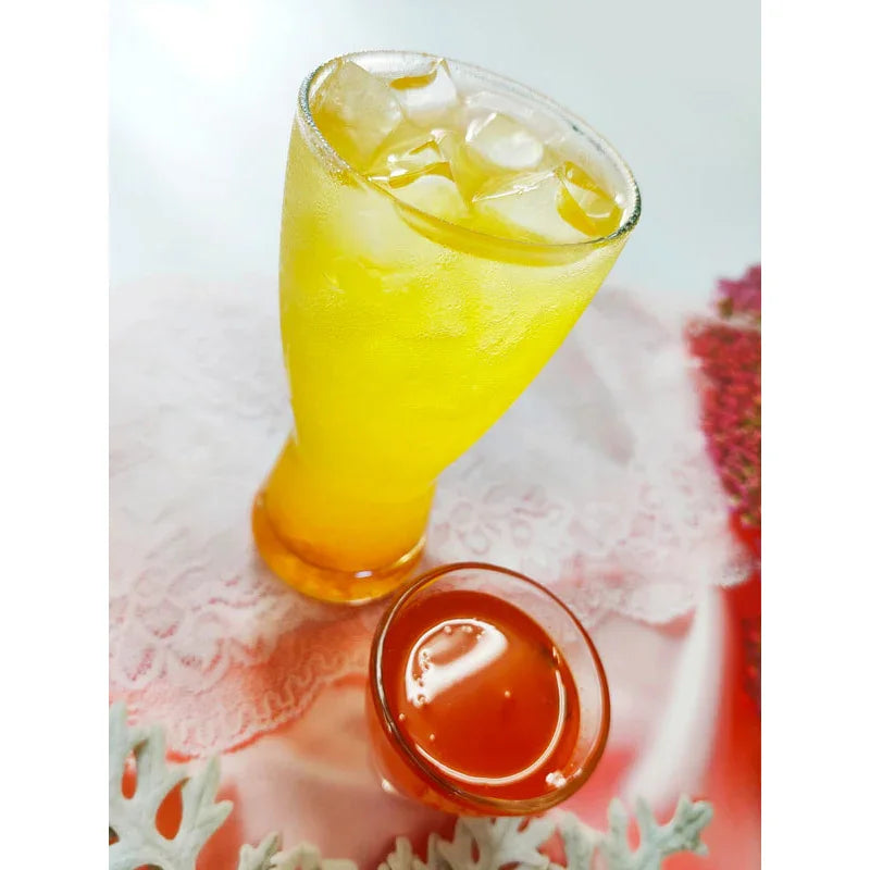 Verre de boisson fraîche jaune avec glaçons et petit verre de sirop orange sur nappe blanche