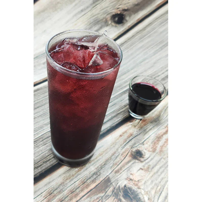 Grand verre de sirop de myrtille glacé sur table en bois avec petite verrine de sirop foncé