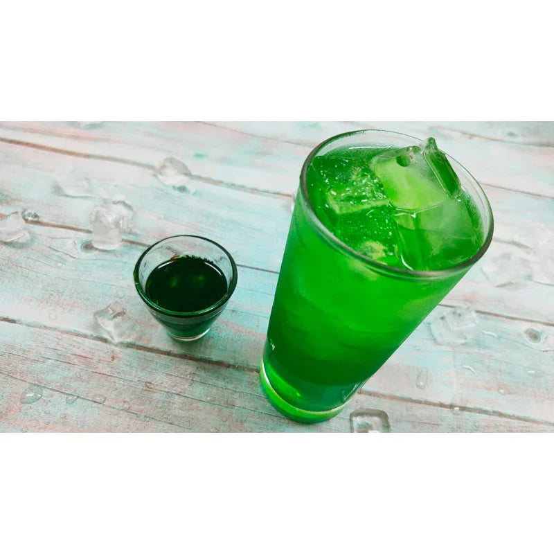 Verre de boisson glacée verte pomme avec glaçons et petit verre de sirop vert sur table en bois clair