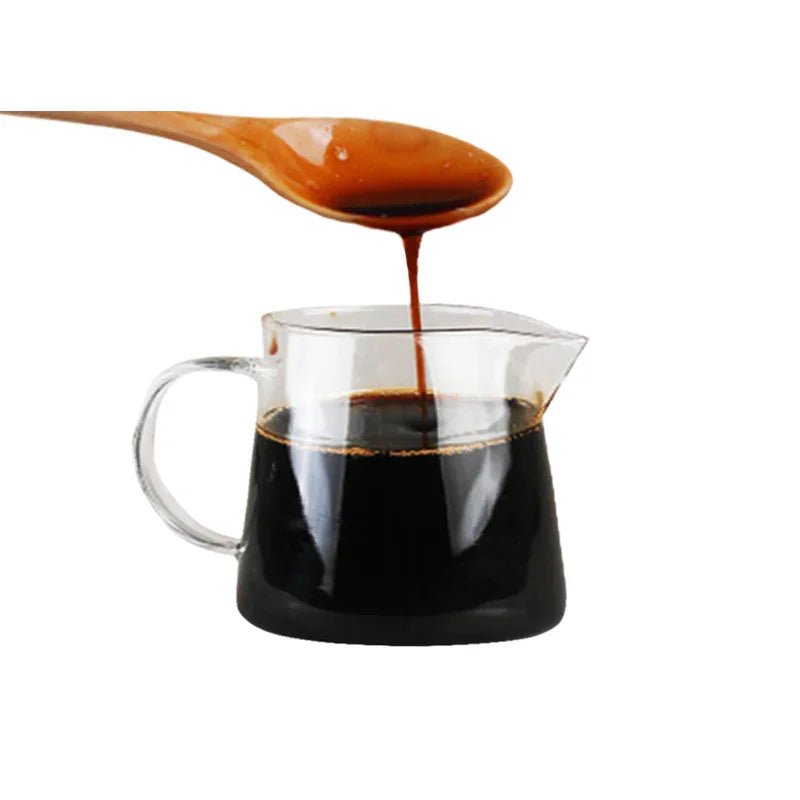 Wooden spoon pouring thick brown syrup into glass measuring cup filled with dark liquid