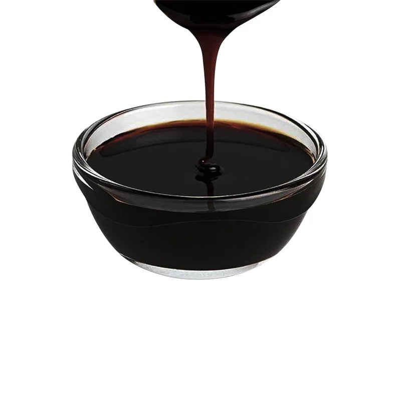 Sauce soja épaisse noire versée dans un bol en verre transparent sur fond blanc