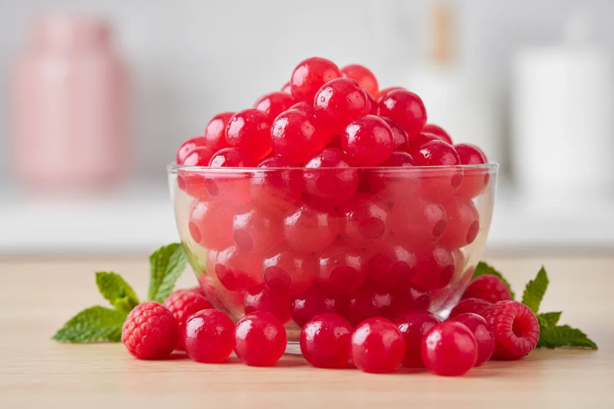Boules translucides rouges dans un bol en verre avec framboises et feuilles de menthe